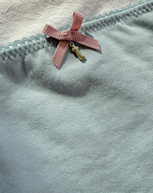 Close-up detail of Teysha organic cotton picot edge bikini brief in dusty blue — delicate scalloped trim and pink bow, GOTS-certified for tween girls