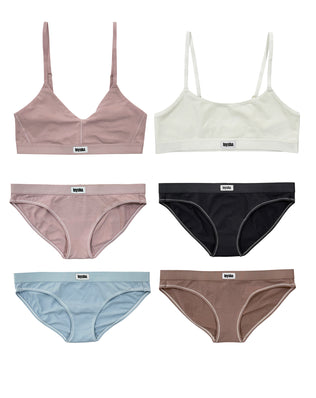 First Bra Starter Pack flat lay — two GOTS-certified organic cotton training bras (dusty pink, cloud white) with four matching hipster briefs in pink, black, blue and natural brown by Teysha, designed for tween girls